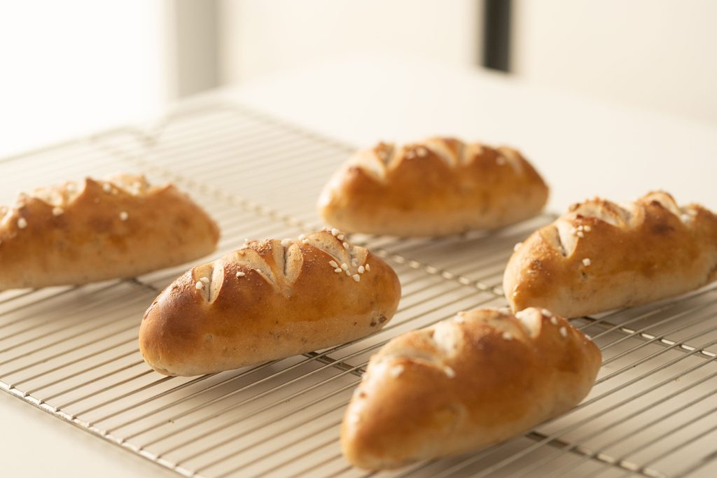 Small crusty bread rolls cooling on a wire rack by a window