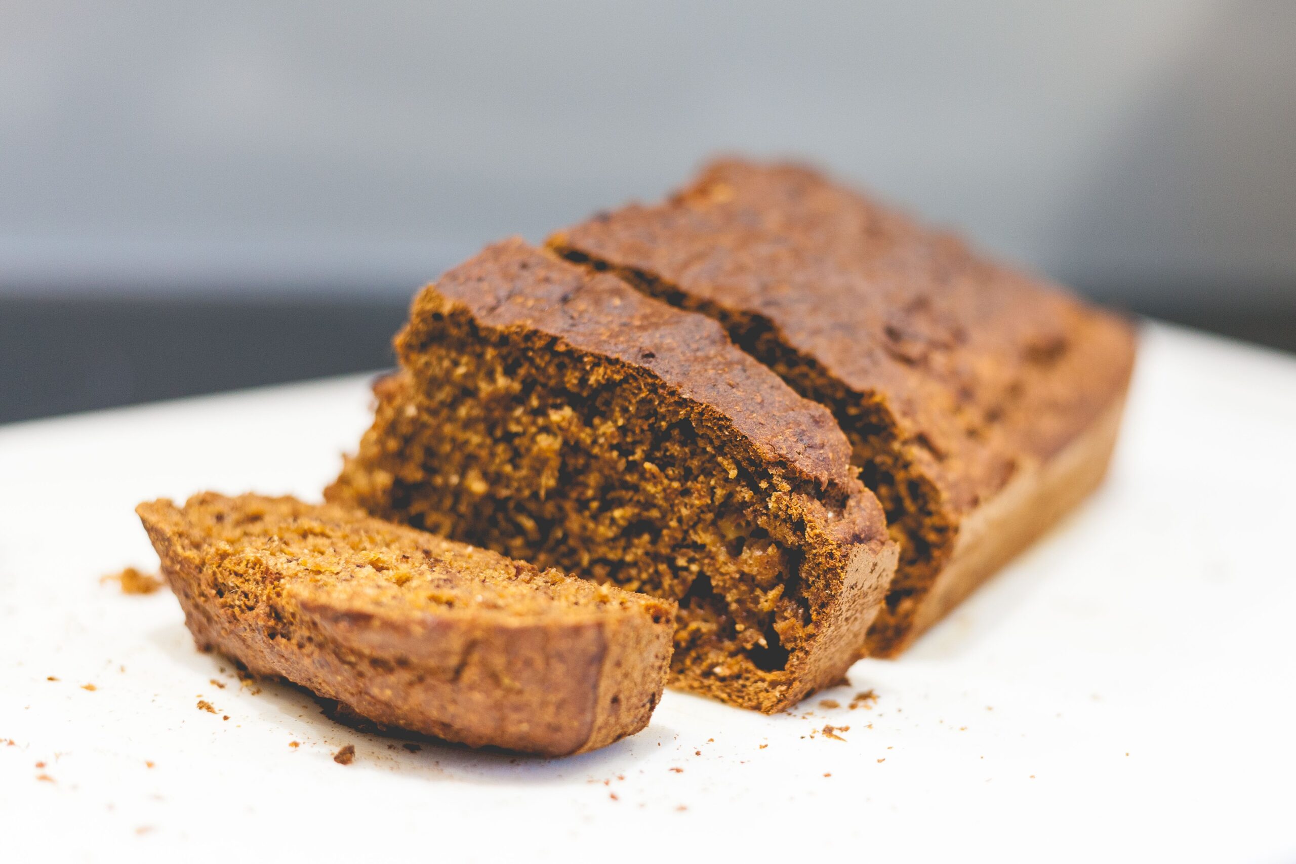 Sliced banana bread loaf on a white surface with crumbs scattered around it