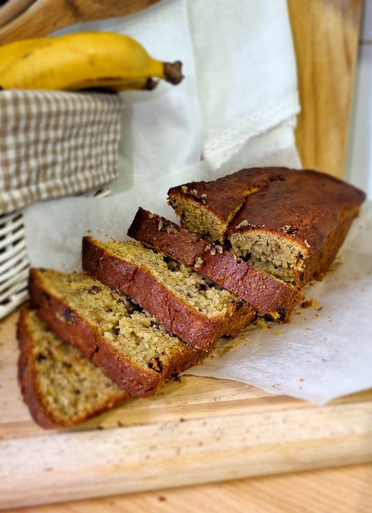 Banana bread cut into thick slices on parchment paper on a wooden board, a banana behind it