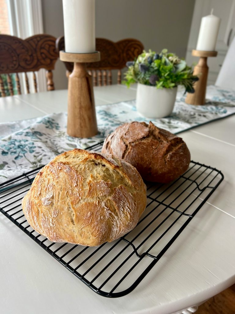 Two round sourdough loaves cooling on a wire rack on a kitchen table